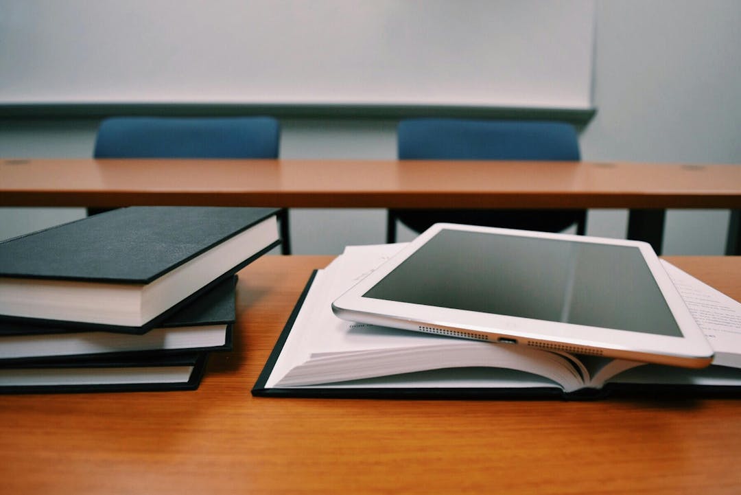 in ipad on top of books placed on a classroom desk