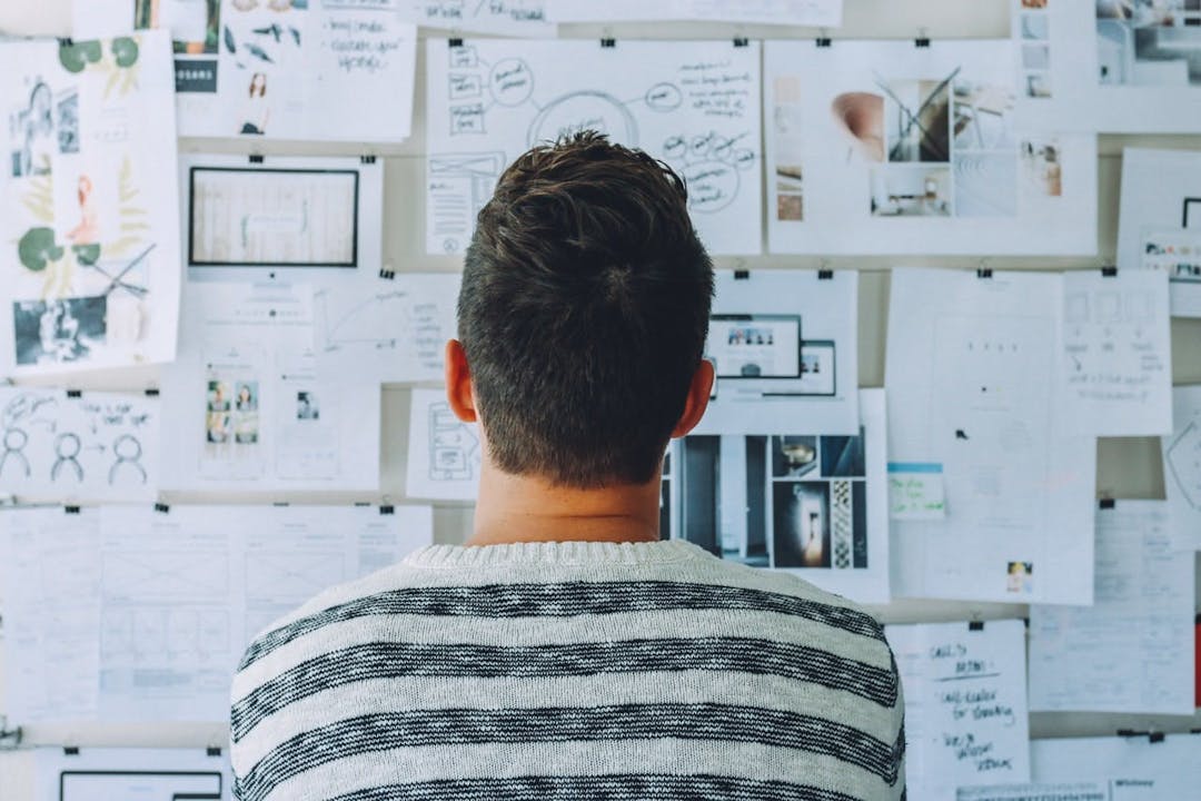 man facing a cork board filled with paper