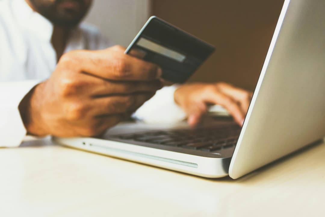 A person holding a credit card while typing on a laptop, preparing to make an online transaction. The image emphasizes digital payments and e-commerce.