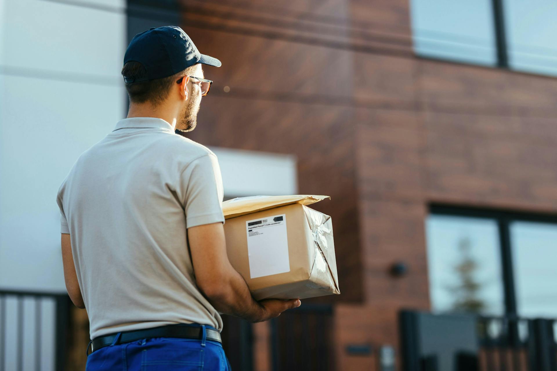 Back view of delivery man walking down the street while carrying packages for a delivery.