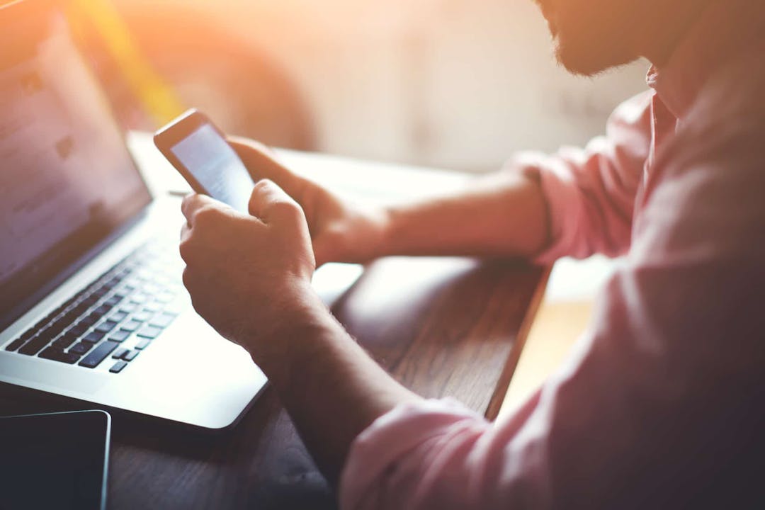 man holding a phone with a laptop on the table